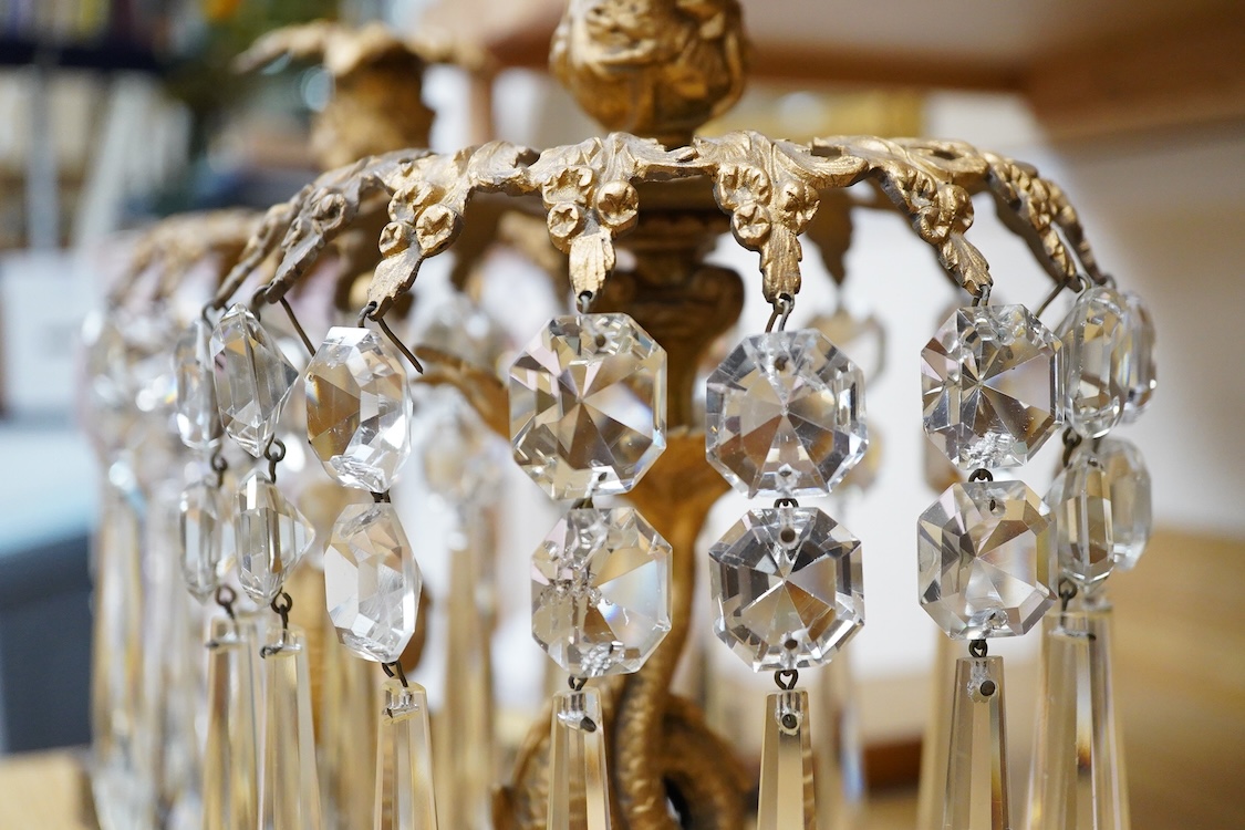 A pair of William IV gilt metal candlesticks, the stems formed as dolphins, with glass lustre drops, raised on square slate bases, 37cm high